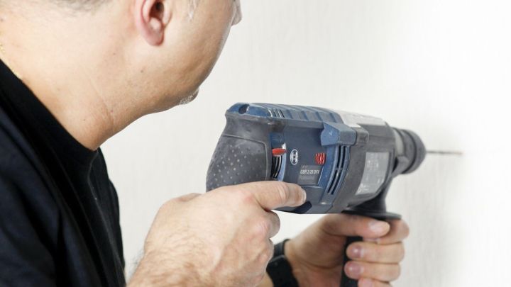 Ein Handwerker verwendet einen Steinbohrer, um ein Loch in eine Wand zu bohren. Die Umgebung ist schlicht und neutral.