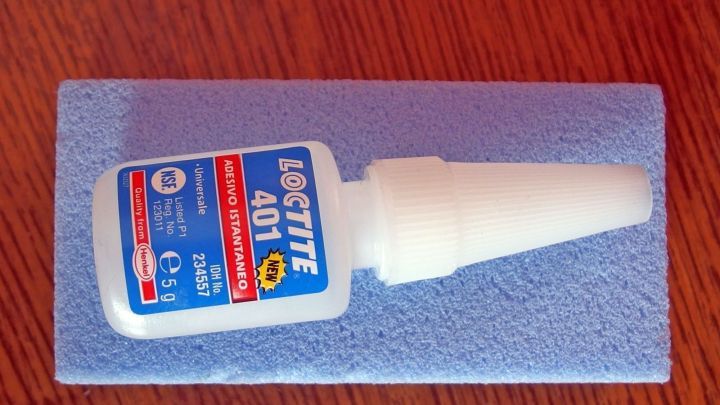 Ein Bimsstein liegt auf einem Holzuntergrund, w&auml;hrend daneben eine Flasche Sekundenkleber deutlich sichtbar ist.