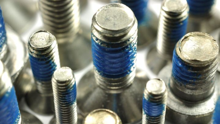Eine Ansammlung von Schrauben mit blauer Schraubensicherung, die auf einer gl&auml;nzenden Oberfl&auml;che pr&auml;sentiert werden.
