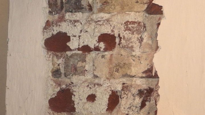 Eine wand mit unregelm&auml;&szlig;igem, abbl&auml;tterndem Mauerm&ouml;rtel aus Klinker und einem wei&szlig;en, glatten Hintergrund.