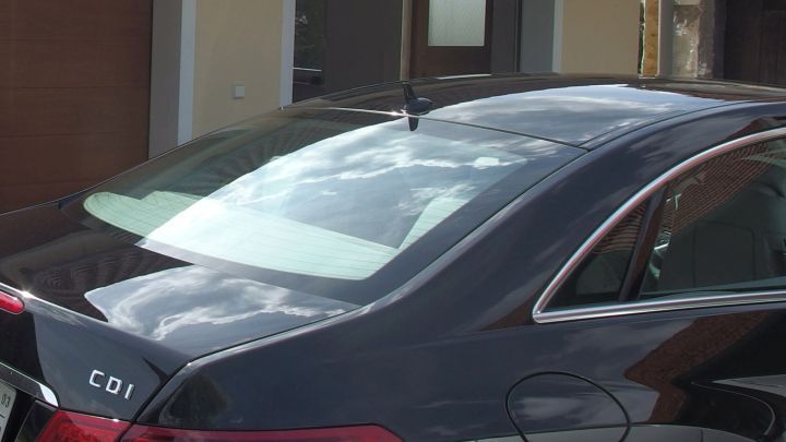 Ein schwarzes Auto steht vor einem Wohnhaus, mit T&ouml;nungsfolie an den Fenstern, die das Licht reflektiert.