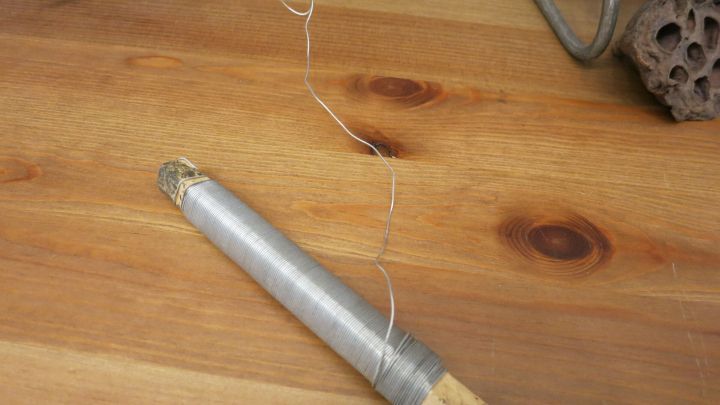 Ein gewickelter Draht wird um einen Gegenstand aus Holz und Metall geformt, der auf einer Holzoberfl&auml;che liegt.