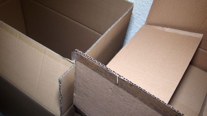 Kartons stehen auf dem Boden, einer ist aufrecht, w&auml;hrend ein anderer gerade ge&ouml;ffnet wird, bereit f&uuml;r den Umzug.