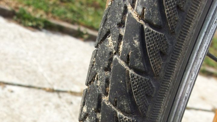 Ein abgenutzter Fahrradreifen liegt auf dem Boden, w&auml;hrend er im Freien auf einem Gehweg betrachtet wird.