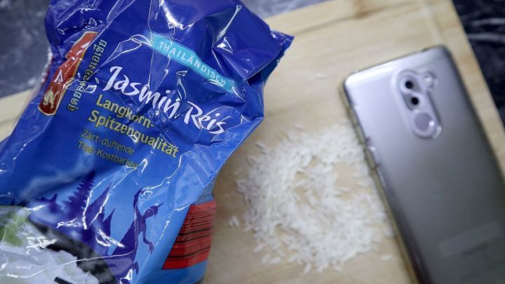 Ein nasses Handy liegt neben Reis auf einem Brett. Links eine ge&ouml;ffnete Jasminreis-Packung mit der Aufschrift "Langkorn-Spitzenqualit&auml;t".