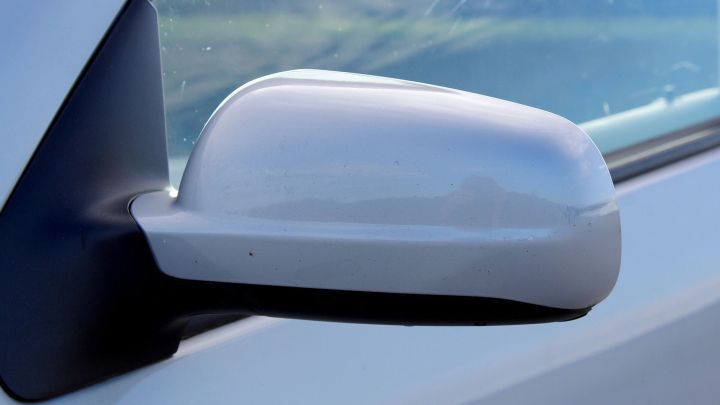 Ein blinkerfreier R&uuml;ckspiegel ist an der Seite eines Autos montiert und reflektiert die Umgebung bei Tageslicht.