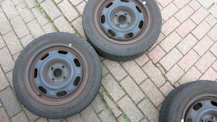 Drei Reifen liegen auf einem Kiesboden, bereit zur Montage an einem Reifenhalter in der Garagenwand.