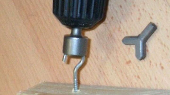 Bohrmaschine dreht Schraubhaken in ein Holzbrett ein, daneben liegt ein kleiner Schl&uuml;ssel auf hellem Holztisch.