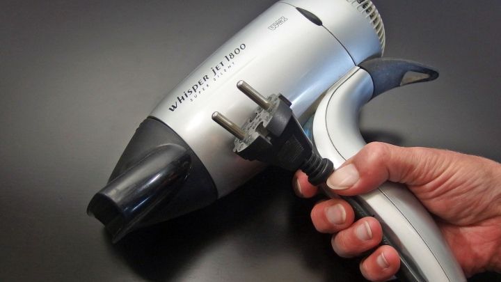 Ein Haartrockner wird in der Hand gehalten. Der Nutzer bereitet sich darauf vor, das Kabel richtig aufzuwickeln, um Ordnung zu schaffen.