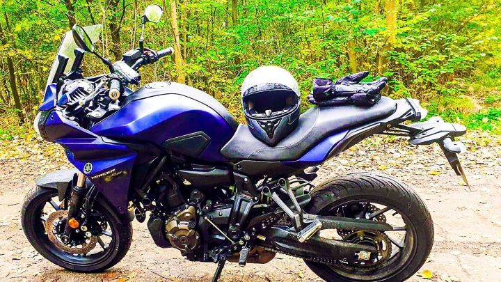 Ein Motorrad steht auf einem Waldweg, w&auml;hrend ein Helm und Handschuhe auf dem Sitz liegen. Die Umgebung ist gr&uuml;n und herbstlich.