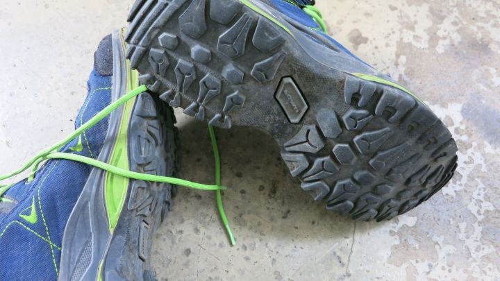 Ein Paar blaue Sportschuhe zeigt die Gummisohlen, die gl&auml;nzen, w&auml;hrend sie auf einem rauen, grauen Boden stehen.