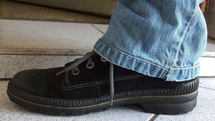 Eine schwarze Schuh und eine Jeans zeigen die Kombination von Hosenl&auml;nge und Schuhwerk in einem Innenraum.