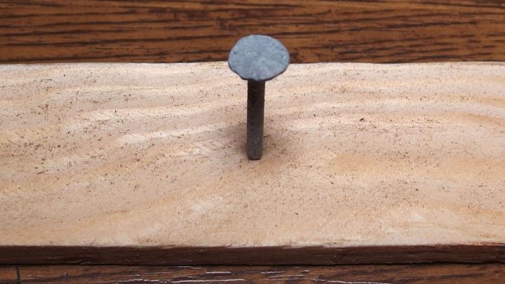 Ein Nagel steht senkrecht in einem St&uuml;ck d&uuml;nnem Holz, das auf einer Holzoberfl&auml;che liegt, ohne dass das Holz splittert.