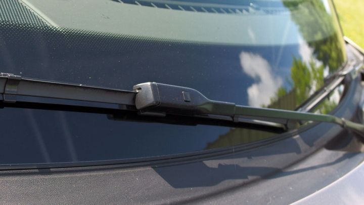 Ein Scheibenwischer reinigt die Frontscheibe, sichtbar in einer klaren Umgebung mit Sonnenlicht und blauem Himmel.