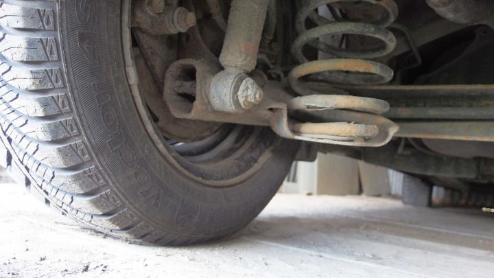 Ein Auto zeigt die Unterseite mit Feder und Reifen, w&auml;hrend der Kontext auf eine ungepflegte Waschstation hinweist.