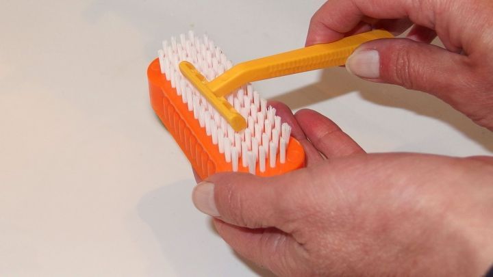 Eine Hand h&auml;lt eine orangefarbene Rasierklingenreinigungsb&uuml;rste und entfernt sorgf&auml;ltig Haare von den Klingen.