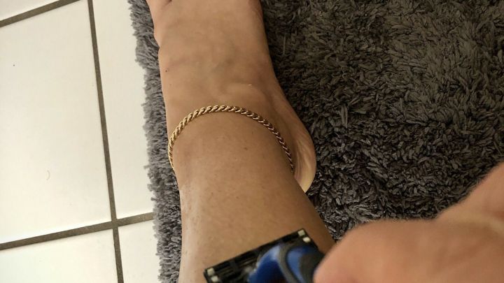 Eine Hand h&auml;lt einen Rasierer, der &uuml;ber das Bein gleitet, w&auml;hrend sich das Fu&szlig; und ein Teppich im Hintergrund befinden.