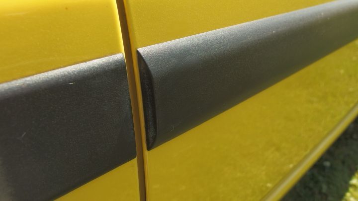 Eine schwarze Kunststoffleiste am Auto wird aufgefrischt, während sich eine gelbe Karosserie im Hintergrund zeigt.