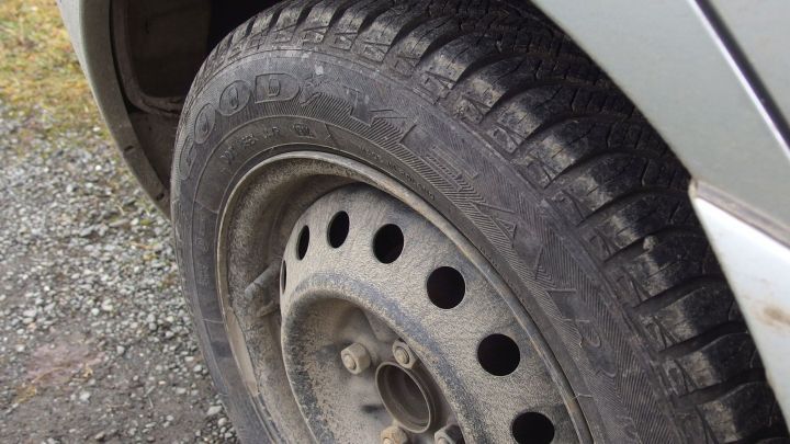 Ein Reifen liegt auf einem Schotterweg, zeigt Abnutzungsspuren und ist auf einem Fahrzeug montiert, das sich in Bewegung befindet.