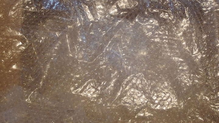 Eine durchsichtige Noppenfolie liegt flach auf einem Tisch, um das Auto vor Hagelschlag zu sch&uuml;tzen.