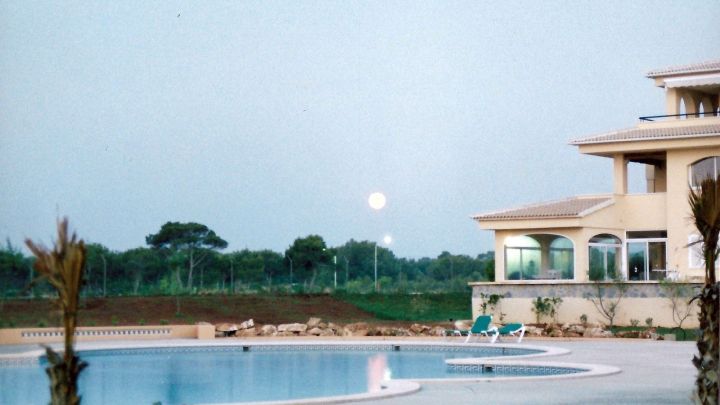 Ein eleganter (Klein-)Pool reflektiert das Licht des Mondes, umgeben von einer modernen Villa und einer ruhigen Landschaft.