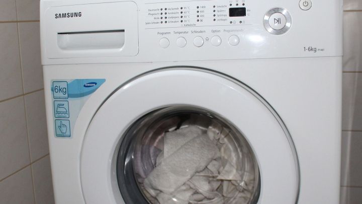 Eine Waschmaschine steht an ihrem Platz und zeigt die W&auml;sche im Fenster, umgeben von hellen Fliesen in einem Badezimmer.