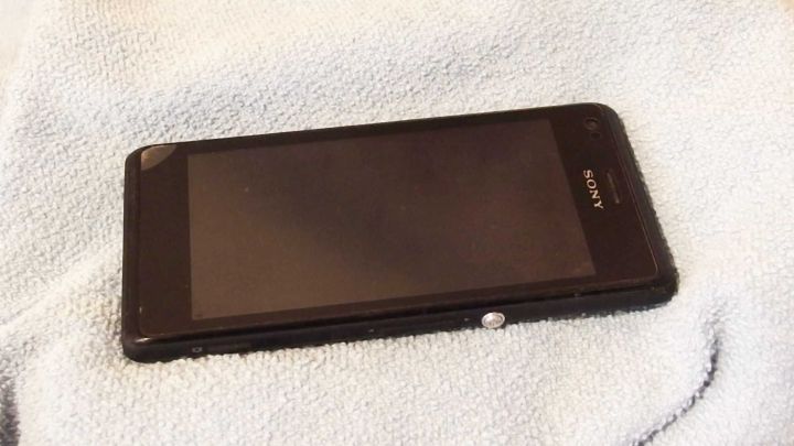 Ein schwarzes Smartphone liegt auf einem Handtuch, nachdem es ins Wasser gefallen ist und getrocknet wird.