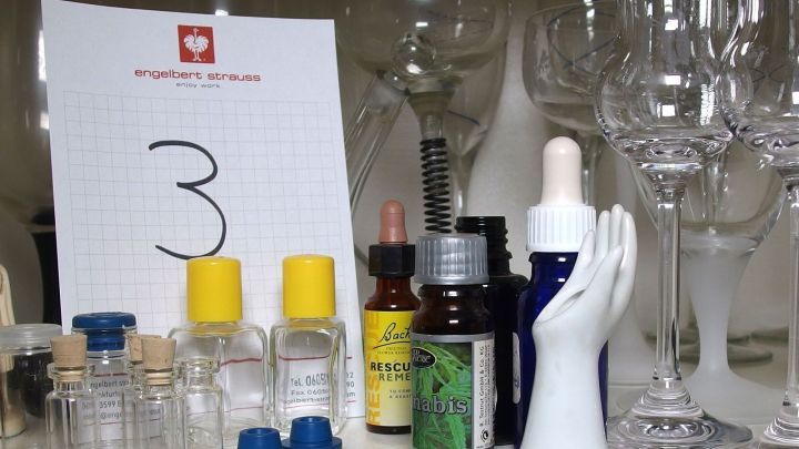 Auf einem Tisch stehen verschiedene Glasbeh&auml;lter, eine Handfigur und ein Nummernschild mit der Zahl 3, umgeben von Glaswaren.