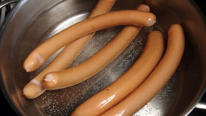 In einem Topf mit hei&szlig;em Wasser schwimmen mehrere Bratw&uuml;rste, die f&uuml;r die Zubereitung zum Verzehr bereit sind.