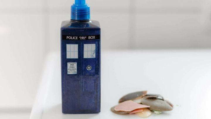 Ein Seifenspender in Form einer blauen Telefonzelle steht neben bunten Seifenresten auf einer wei&szlig;en Oberfl&auml;che.