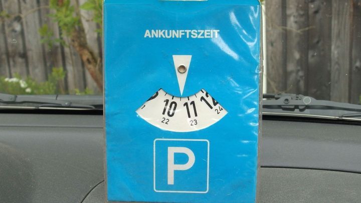 Eine Papp-Parkscheibe steht auf dem Armaturenbrett, während sie auf den Parkzeitpunkt hinweist.
