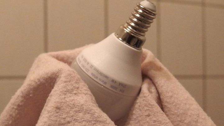 Eine gl&uuml;hende Lampe wird sorgf&auml;ltig mit einem Handtuch gehalten, um Hautkontakt beim Wechseln zu vermeiden.