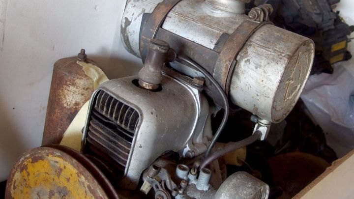 Ein verschmutzter Motor liegt in einem Raum, umgeben von Werkzeugen, wartet darauf, mit &ouml;lverschmierten H&auml;nden gereinigt zu werden.