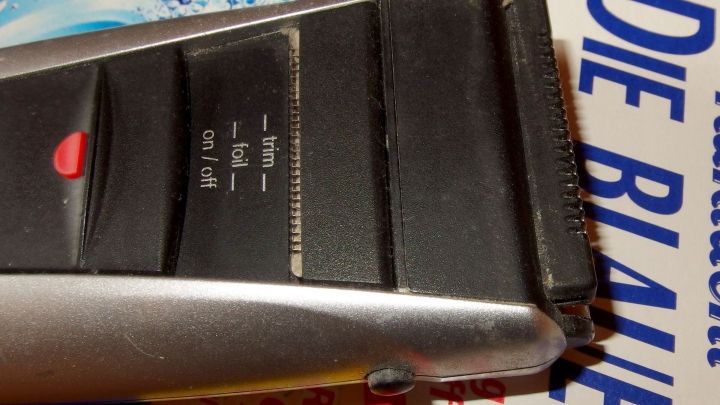 Ein Scheerblatt liegt auf einer Unterlage und wird gereinigt, w&auml;hrend ein Schalter und einige Einstellungen sichtbar sind.