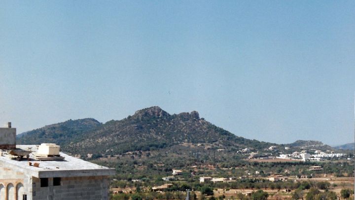 Eine Berglandschaft erhebt sich majest&auml;tisch im Hintergrund, w&auml;hrend ein klarer blauer Himmel &uuml;ber Spanien strahlt.