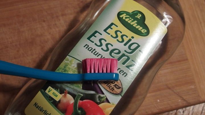 Eine Flasche Essig-Essenz steht auf einer Holzoberfl&auml;che, w&auml;hrend eine Zahnb&uuml;rste darauf liegt, bereit zur Anwendung gegen Nagelpilz.