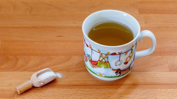 Eine Tasse mit gr&uuml;nem Tee steht neben einem kleinen Beh&auml;lter mit Salz auf einem Holztisch.