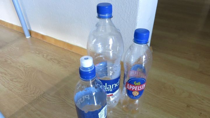 Eine Gruppe von leeren Wasserflaschen steht auf einem Holzboden, w&auml;hrend jemand an der Decke bohrt, um Schmutz zu vermeiden.