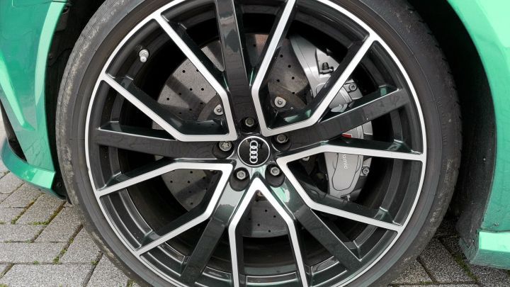 Eine Autosfelge gl&auml;nzt nach der Reinigung, umgeben von einer gr&uuml;nen Karosserie, die frisch poliert aussieht.