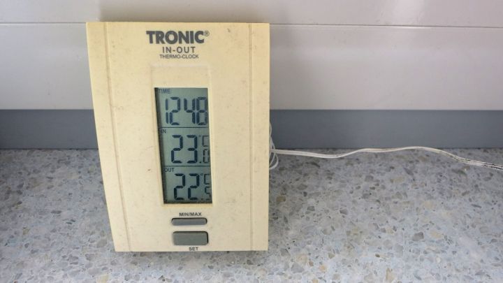 Thermo-Uhr zeigt Zeit (12:48), Innentemperatur (23,8&deg;C) und Au&szlig;entemperatur (22,9&deg;C) an, kabelgebunden auf grauem Boden.