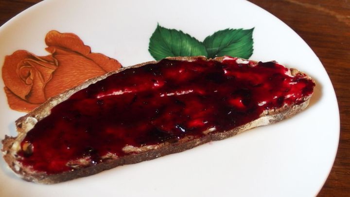 Eine Scheibe Brot mit Marmelade liegt auf einem Teller mit Rosenmuster, auf einem Holztisch platziert.