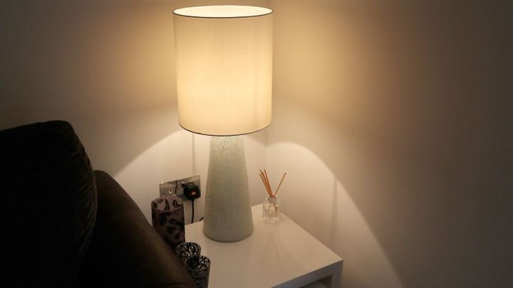 Eine stilvolle Lampe strahlt sanftes Licht aus und beleuchtet eine helle Wand neben einem modernen Beistelltisch.