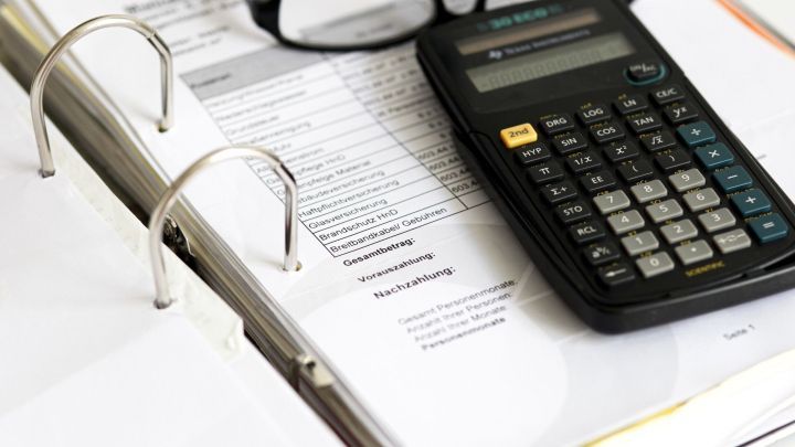 Ein Taschenrechner liegt auf einer ordentlichen Liste mit Nebenkosten, w&auml;hrend eine Brille daneben platziert ist.