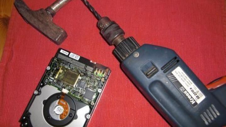 Eine Festplatte liegt auf einem roten Tisch, neben einem Bohrer und einem Hammer, bereit zur sicheren Entsorgung.