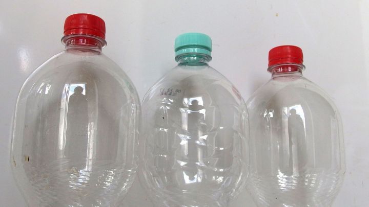 Drei leere Plastikflaschen mit verschiedenen Farben der Verschl&uuml;sse stehen auf einem hellen Hintergrund und warten auf Pfandgeld.