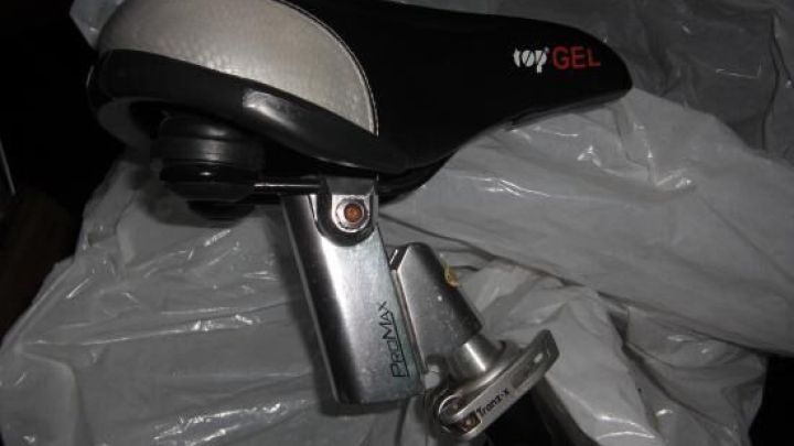 Ein Fahrradsattel mit schwarzer, gepolsterter Oberfl&auml;che und "Gel"-Schriftzug liegt auf einer wei&szlig;en Plastikplane. Text: "Promax", "Top Gel".