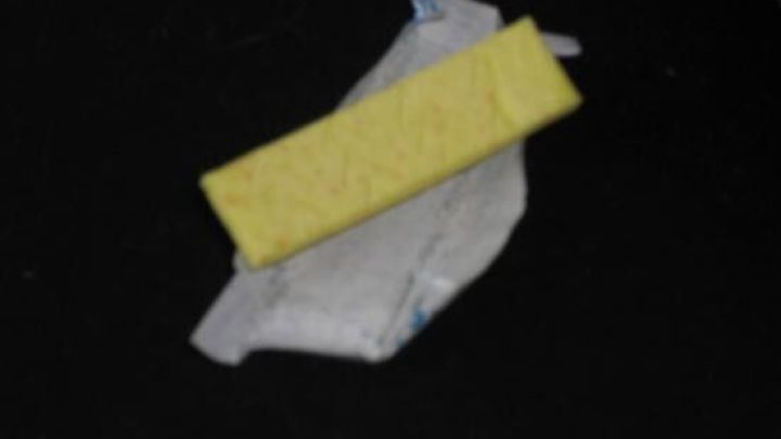 Ein gelber Kaugummi liegt auf offenem Papier auf einer dunklen Oberfl&auml;che.