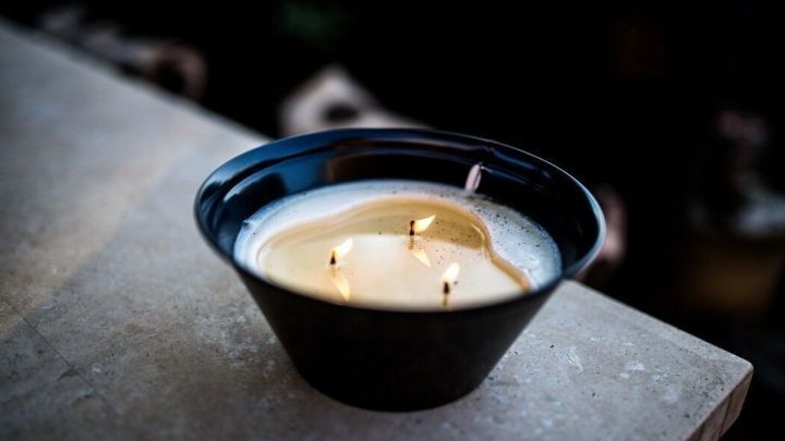Eine schwarze Schale mit geschmolzenem Kerzenwachs steht auf einer Oberfl&auml;che, umgeben von einem dunklen Hintergrund.