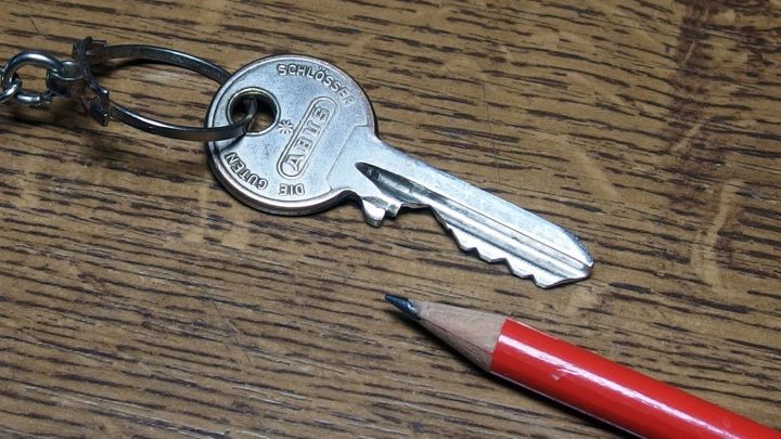 Ein Schl&uuml;ssel liegt auf einem Holztisch, w&auml;hrend ein Bleistift daneben liegt, bereit, um Graphit aufzutragen und zu schmieren.