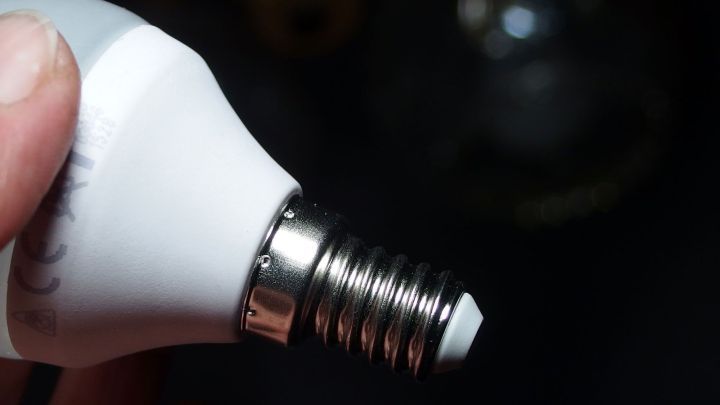 Eine Hand h&auml;lt eine Gl&uuml;hbirne, die kurz vor dem Eindrehen in eine Fassung ist, in einem dunklen Raum.